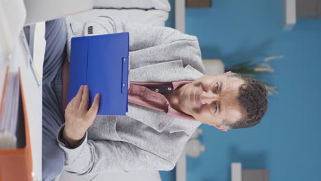 Vertical-video-of-Home-office-worker-old-man-smiling-at-camera-looking-at-paperwork.